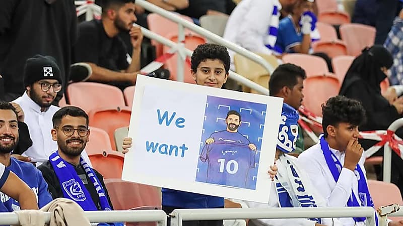 مشجع هلالي يرفع لافتة مكتوب عليها "نحن نريد ميسي" خلال مباراة الهلال والاتحاد